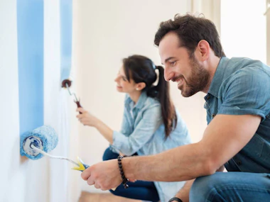 A man and a woman painting a wall blue.